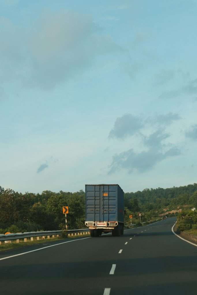A cargo truck driving on an open highway surrounded by nature. Ample copy space available.