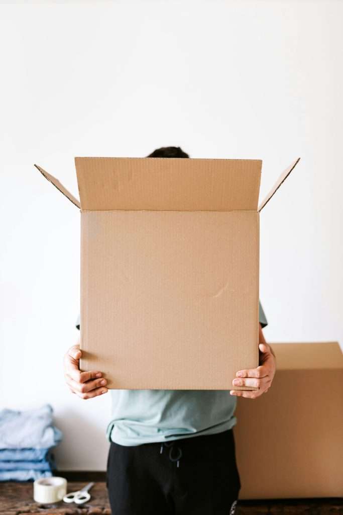 Faceless individual holding an open cardboard box during a home move.