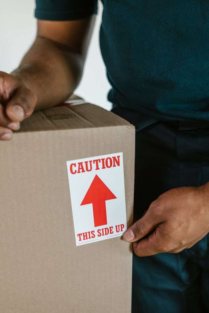 A person handling a moving box with a 'caution this side up' label indoors.